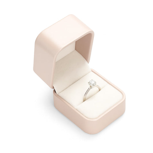 Open blush pink ring box with cream velvet interior holding engagement ring